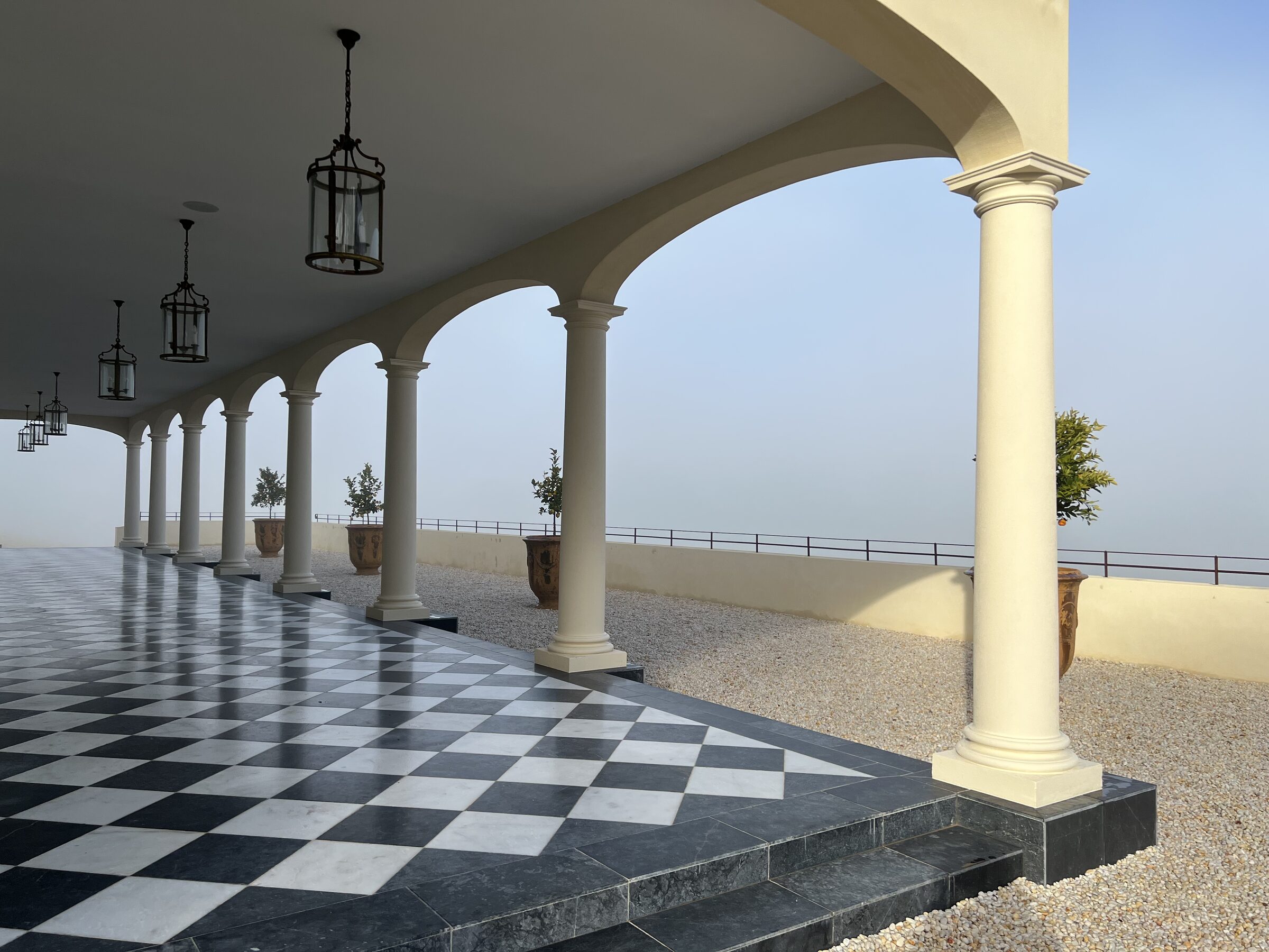 The colonnade at Terre Rouge — arched columns with hanging lanterns and checkerboard floor, looking out into the misty Dandenong Ranges