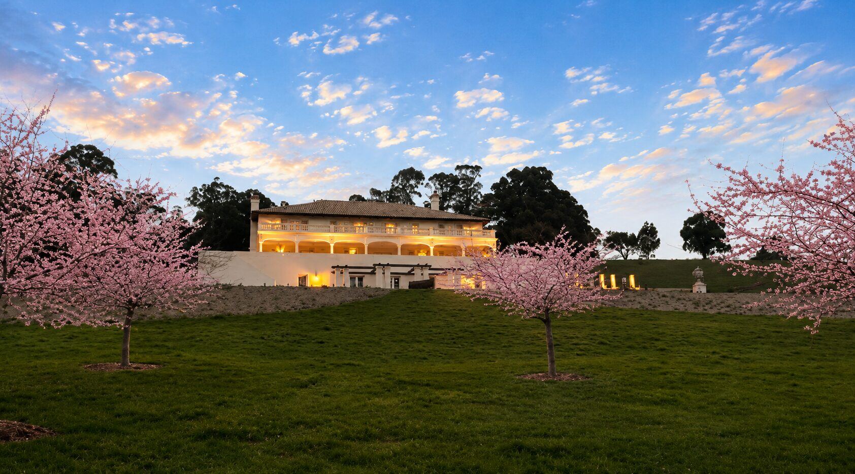 Terre Rouge Estate at dusk with cherry blossoms and the manor lit warm from within
