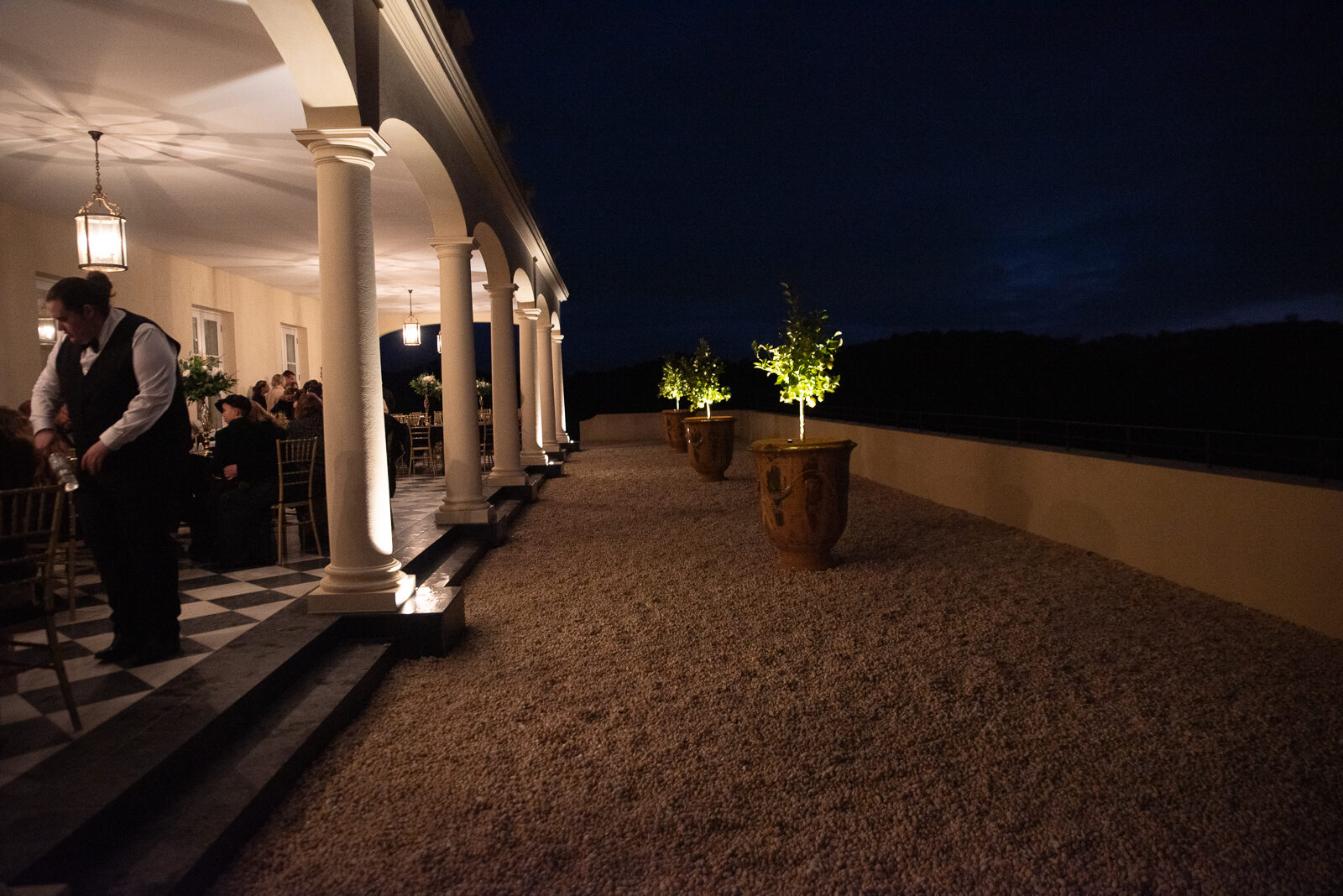 The Terre Rouge terrace at dusk, with reception tables set under the colonnade and lanterns illuminating the evening